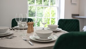 A dining table set with white plates, bowls, and wine glasses, with green upholstered chairs. - Cosy 1BD in Malvern With Stunning Views (Malvern)