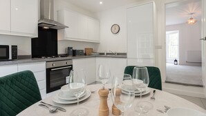 A modern kitchen with white cabinets, a stainless steel range hood, and a dining area with a table set for four. - Cosy 1BD in Malvern With Stunning Views (Malvern)