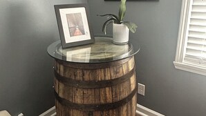 Un tonneau en bois transformé en table, sur lequel on a posé un tableau encadré et un pot de fleurs.