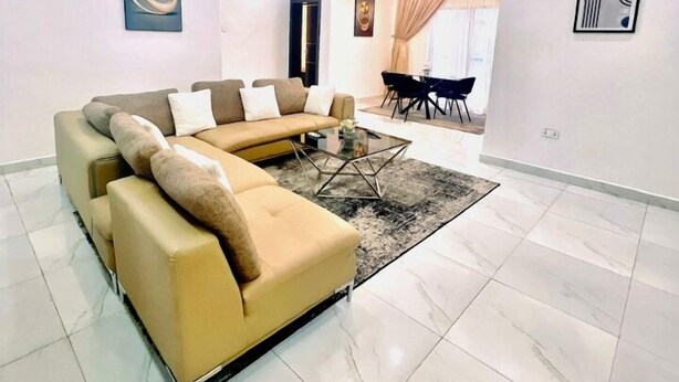 Un salon moderne avec un canapé d’angle, une table basse en verre et un coin repas avec des chaises.