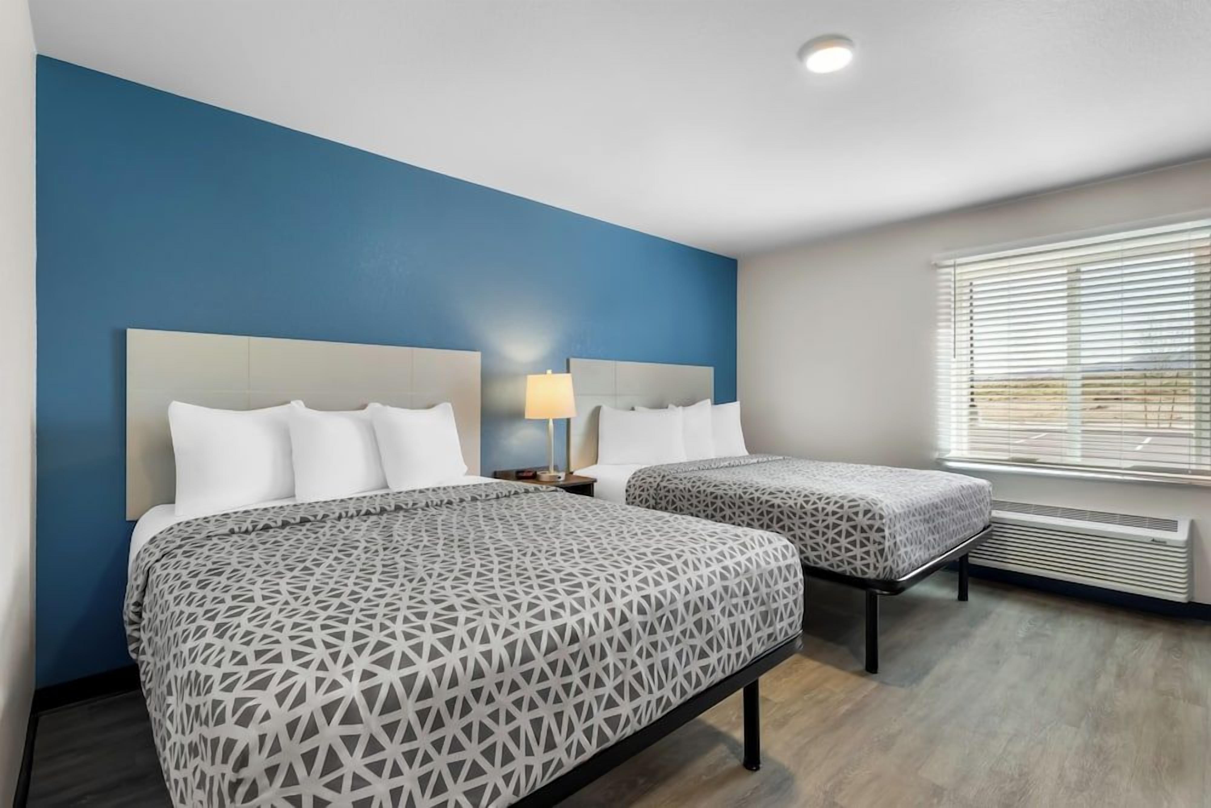A hotel room with two beds, a nightstand with a lamp, and a window with blinds.