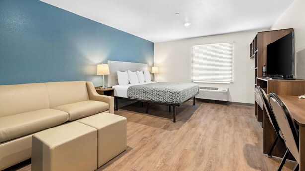 A hotel room with a bed, a sofa, a desk, and a TV. - Woodspring Suites Ceres - Modesto (Ceres)