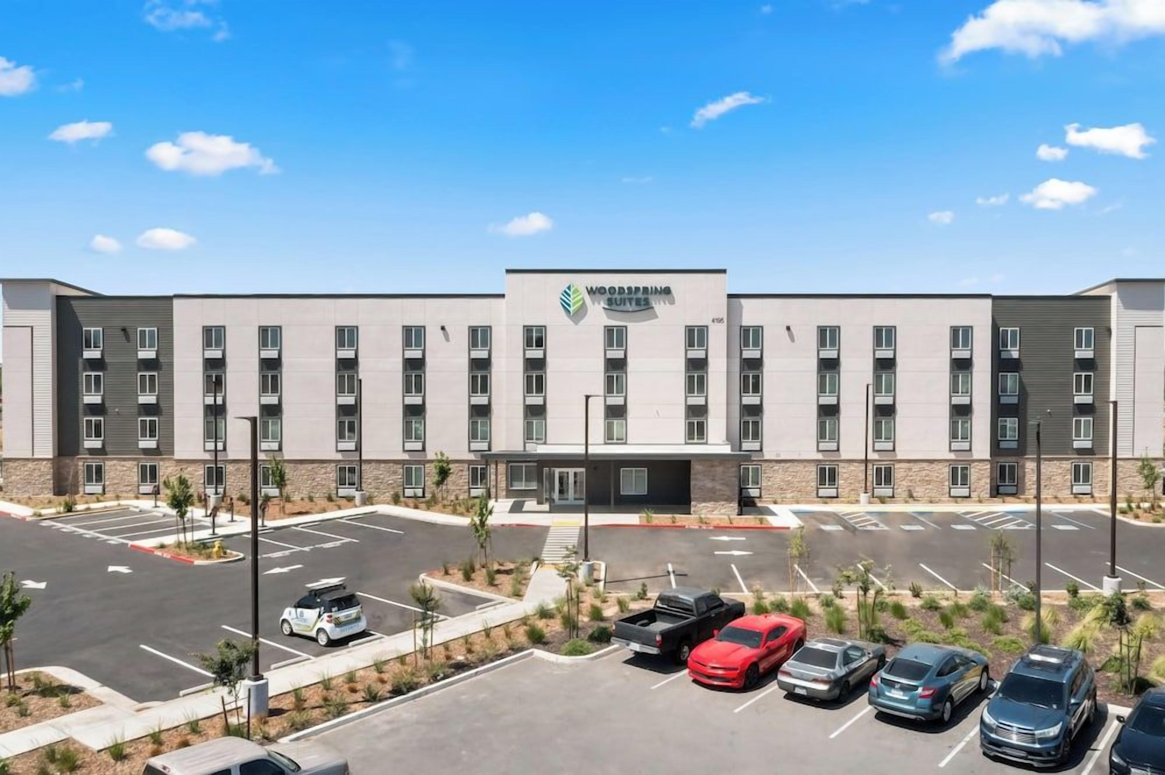 A multi-story hotel with a central entrance, parking lot, and a clear sky.