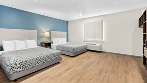 A hotel room with two beds, a nightstand, a lamp, a window with blinds, and a built-in heater. - Woodspring Suites Ceres - Modesto (Ceres)