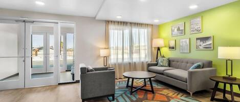 A modern living room with a sofa, armchair, and coffee table, a patterned rug, and a green accent wall with framed pictures.