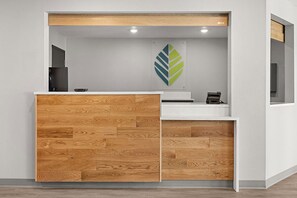 A reception desk with a wooden panel design, a logo on the wall, and a small window.