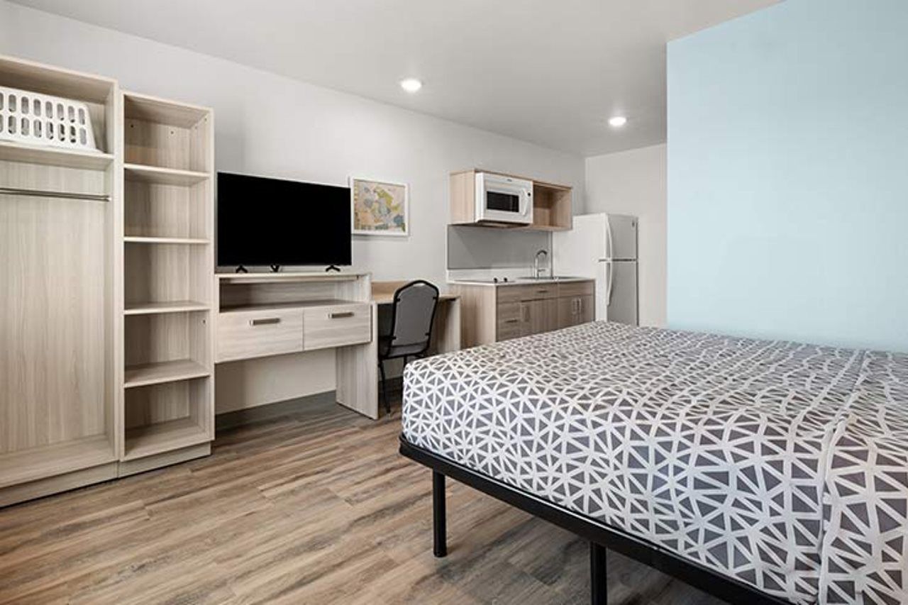 Habitación pequeña con cama, escritorio, silla, televisor, microondas y refrigerador.