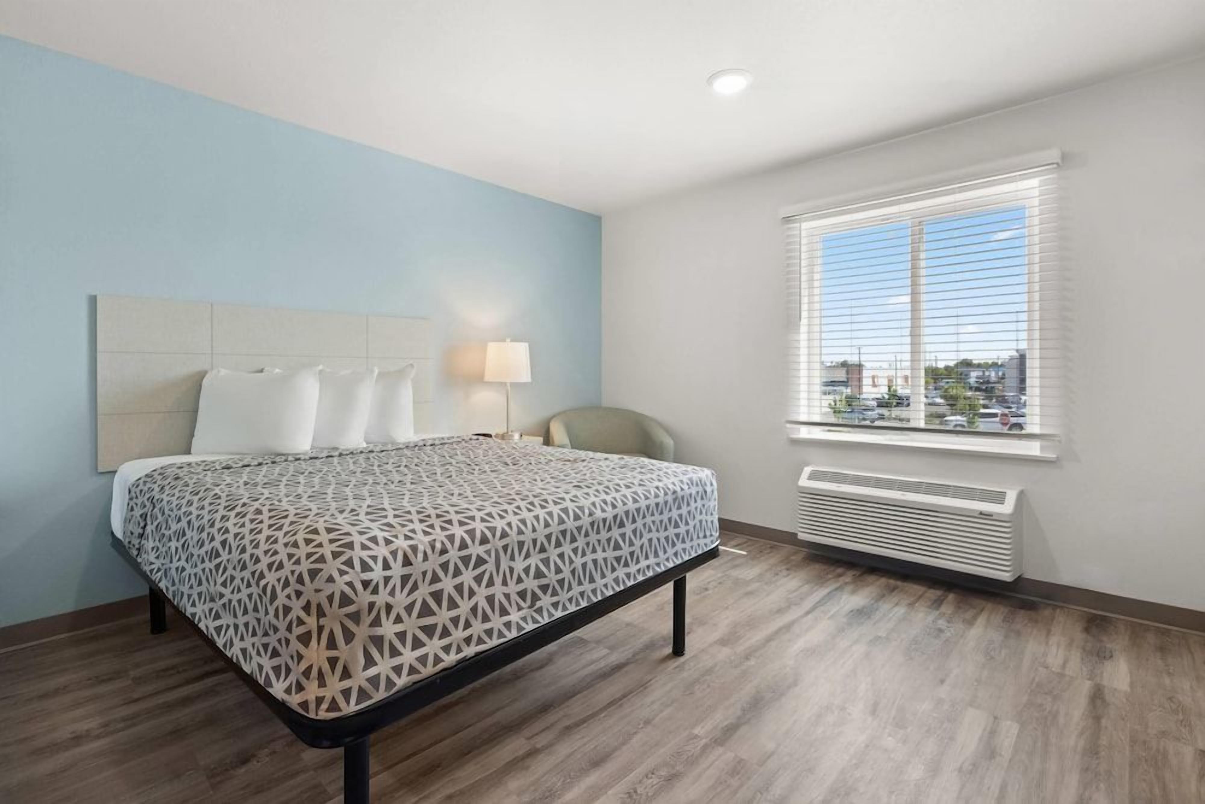 Habitación de hotel con cama, ventana con persianas, radiador y vista a la ciudad.