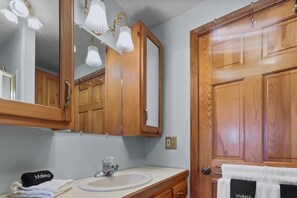 Un baño con armarios de madera, un lavamanos, un espejo y un perchero para toallas.
