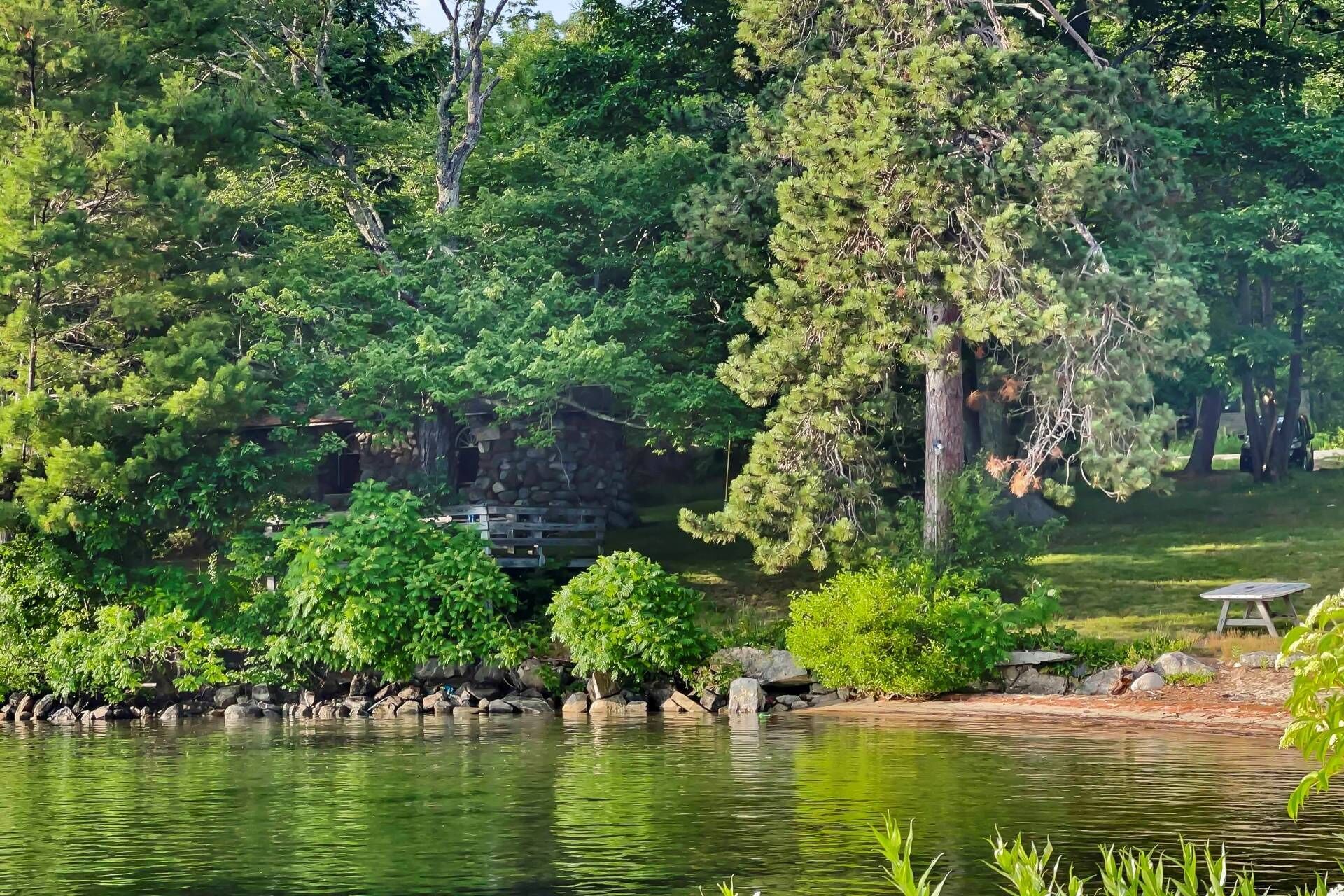 Un entorno tranquilo junto al lago, con abundante vegetación, una estructura de piedra y un muelle de madera.