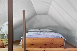 Un pequeño dormitorio en ático con forma triangular, con una cama de madera y ropa de cama blanca.