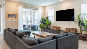 A modern living room with a grey sectional sofa, a wooden coffee table, and a flat-screen TV mounted on the wall.