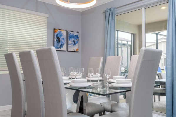 A dining area with a glass table set for six, surrounded by cushioned chairs.