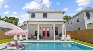 Une maison à deux étages avec un patio couvert, une piscine et une porte rose.