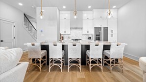 Une cuisine moderne avec des meubles blancs, un îlot central doté de tabourets et des luminaires suspendus.