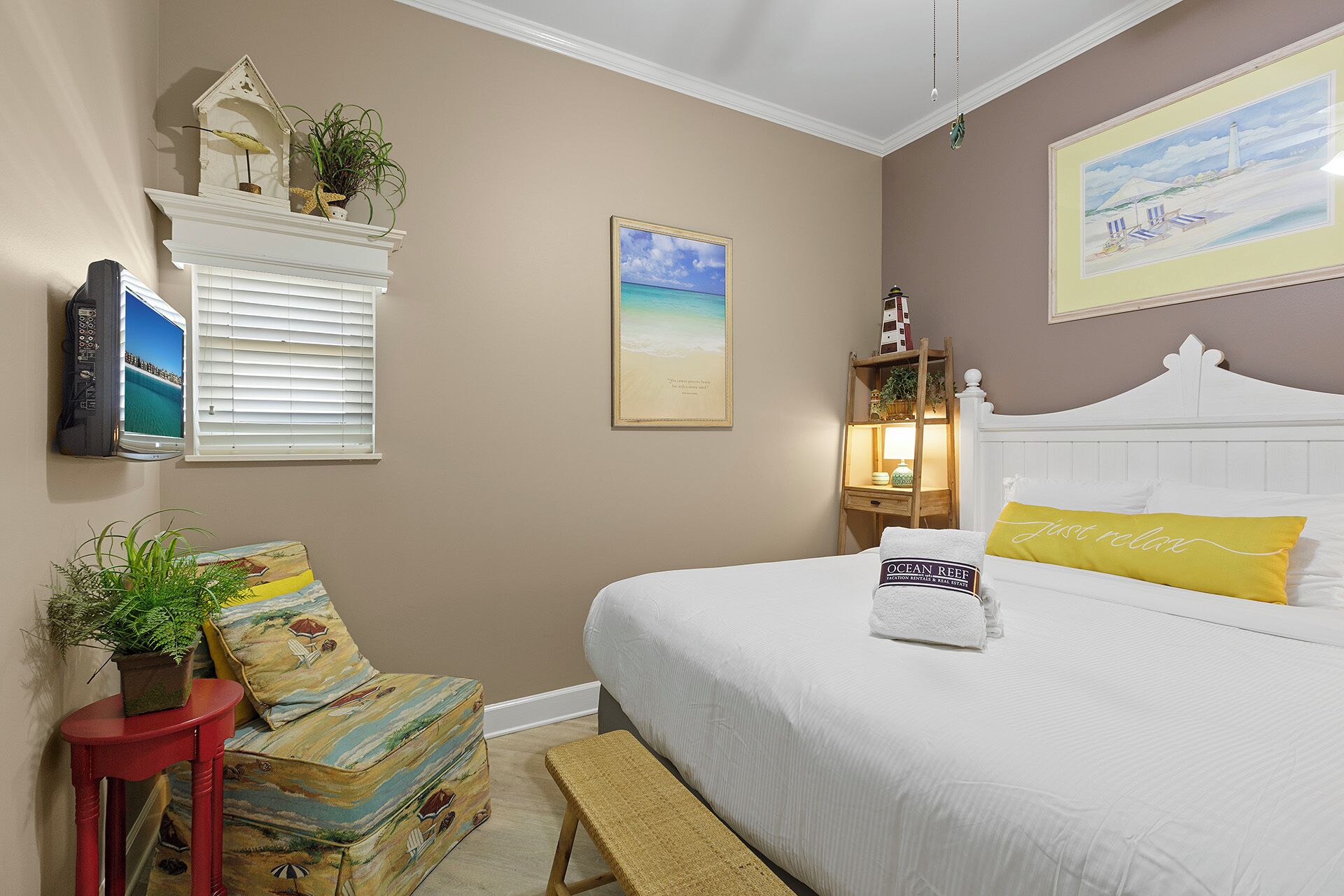 A bedroom with a bed, a television mounted on the wall, a framed picture, and a small table with a plant.