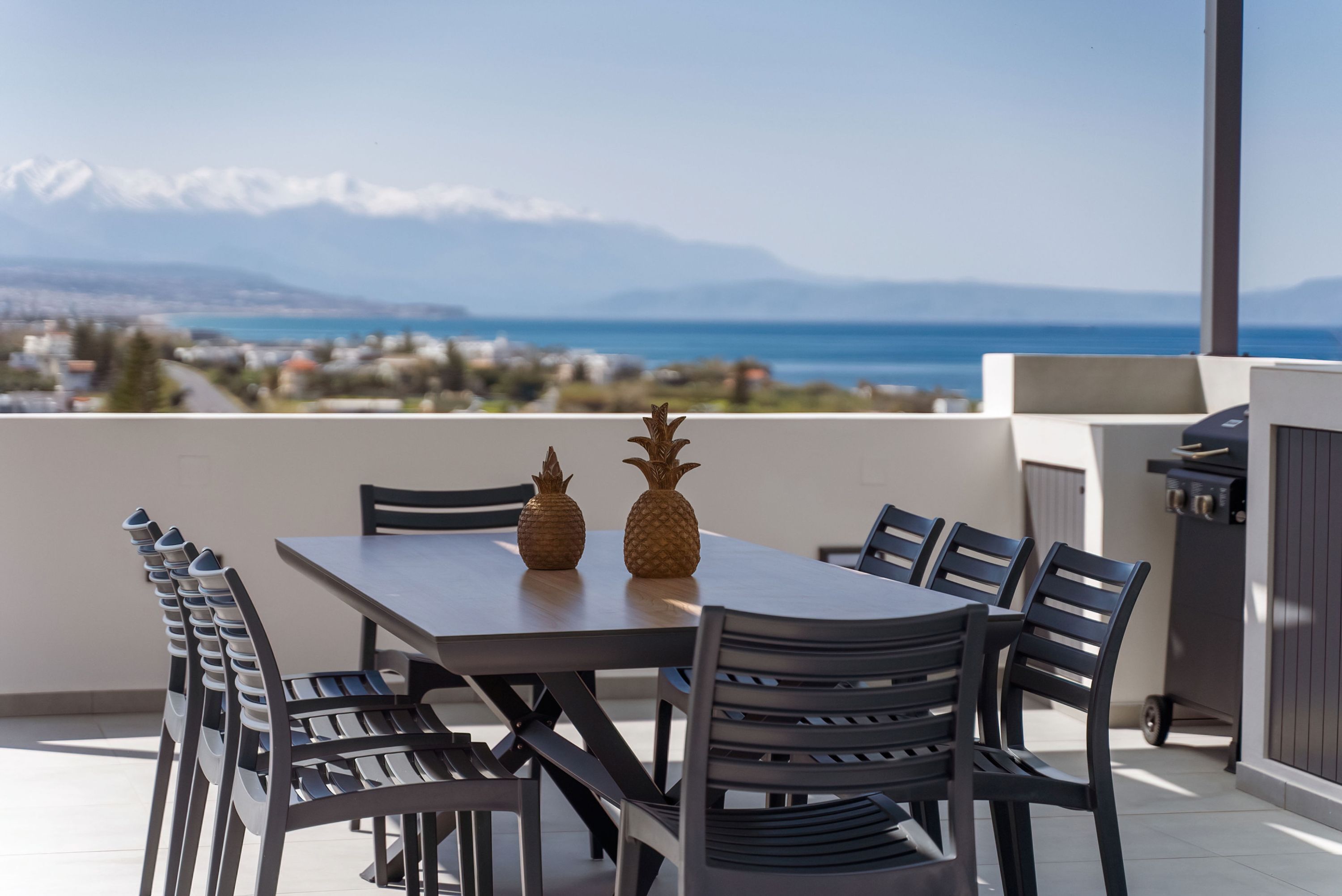 Un comedor con una mesa y sillas, dos centros de mesa con piña y vistas al mar y las montañas de fondo.