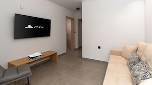 A modern living room with a flat-screen TV mounted on the wall, a wooden bench, a grey chair, and a beige sofa with patterned cushions. - Villa Aelia - With Private Pool and Sauna (Rethymno)