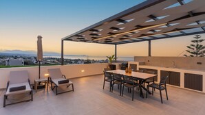 A rooftop terrace with a dining area, lounge chairs, and a view of the city and water. - Villa Aelia - With Private Pool and Sauna (Rethymno)