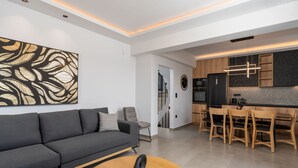 A modern living room with a grey sofa, a round wooden coffee table, and a large abstract painting on the wall. - Villa Aelia - With Private Pool and Sauna (Rethymno)