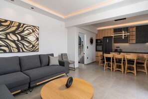 Ein modernes Wohnzimmer mit einem grauen Sofa, einem runden Couchtisch aus Holz und einem großen, abstrakten Gemälde an der Wand.