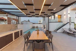 Ein moderner Essbereich im Freien mit Pool, Treppe und Blick auf umliegende Gebäude.