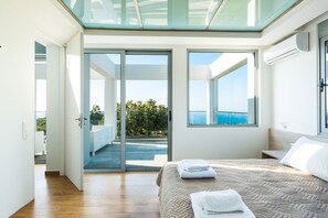 A modern bedroom with a large bed, a glass door leading to a balcony, and a view of the sea. - Villa O2 - With Private Heated Pool (Rethymno)