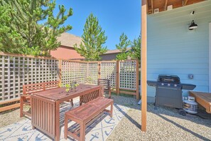 Eine Terrasse im Freien mit einem Holztisch, Bänken, einem Grill und einem Gitterzaun.