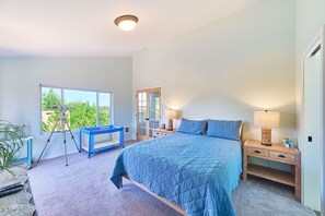 Ein Schlafzimmer mit einem großen Bett, einem Fenster, einem Schreibtisch und einem Teleskop.