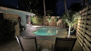 A backyard with a swimming pool, two chairs, a small table, and a wooden fence. - Less than 7 minute walk to Siesta Key Beach. (Sarasota)