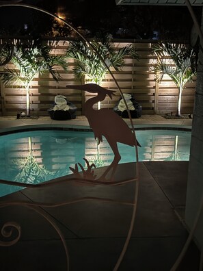 A pool area with a decorative bird sculpture, wooden fence, and potted plants.