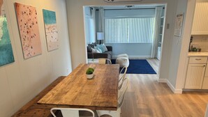 A dining area with a wooden table and white chairs, a small potted plant, and artwork on the wall. - Less than 7 minute walk to Siesta Key Beach. (Sarasota)