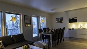 A modern living room with a sofa, dining table, and kitchen area. - Parkstigens Lägenheter (Funasdalen)