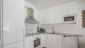 A modern kitchen with white cabinetry, a stainless steel range hood, a built-in microwave, a coffee maker, and a dishwasher. - Parkstigens Lägenheter (Funasdalen)