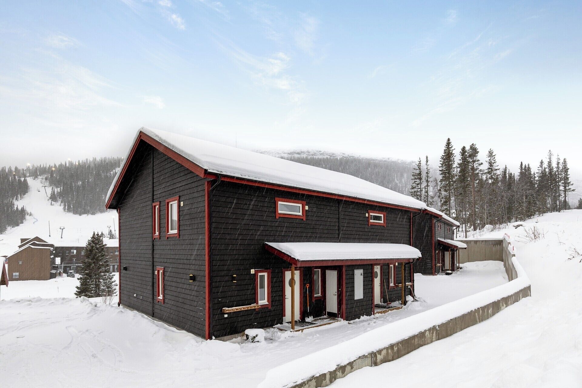 A two-story wooden building with a snow-covered roof, surrounded by a snowy landscape and trees.