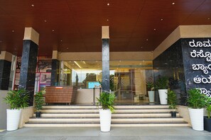 A hotel entrance with marble columns, a reception desk, and potted plants. - Highland Hotel (Bengaluru)