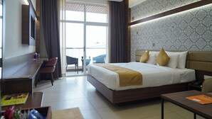 A hotel room with a large bed, a desk, a chair, and a TV. - Highland Hotel (Bengaluru)
