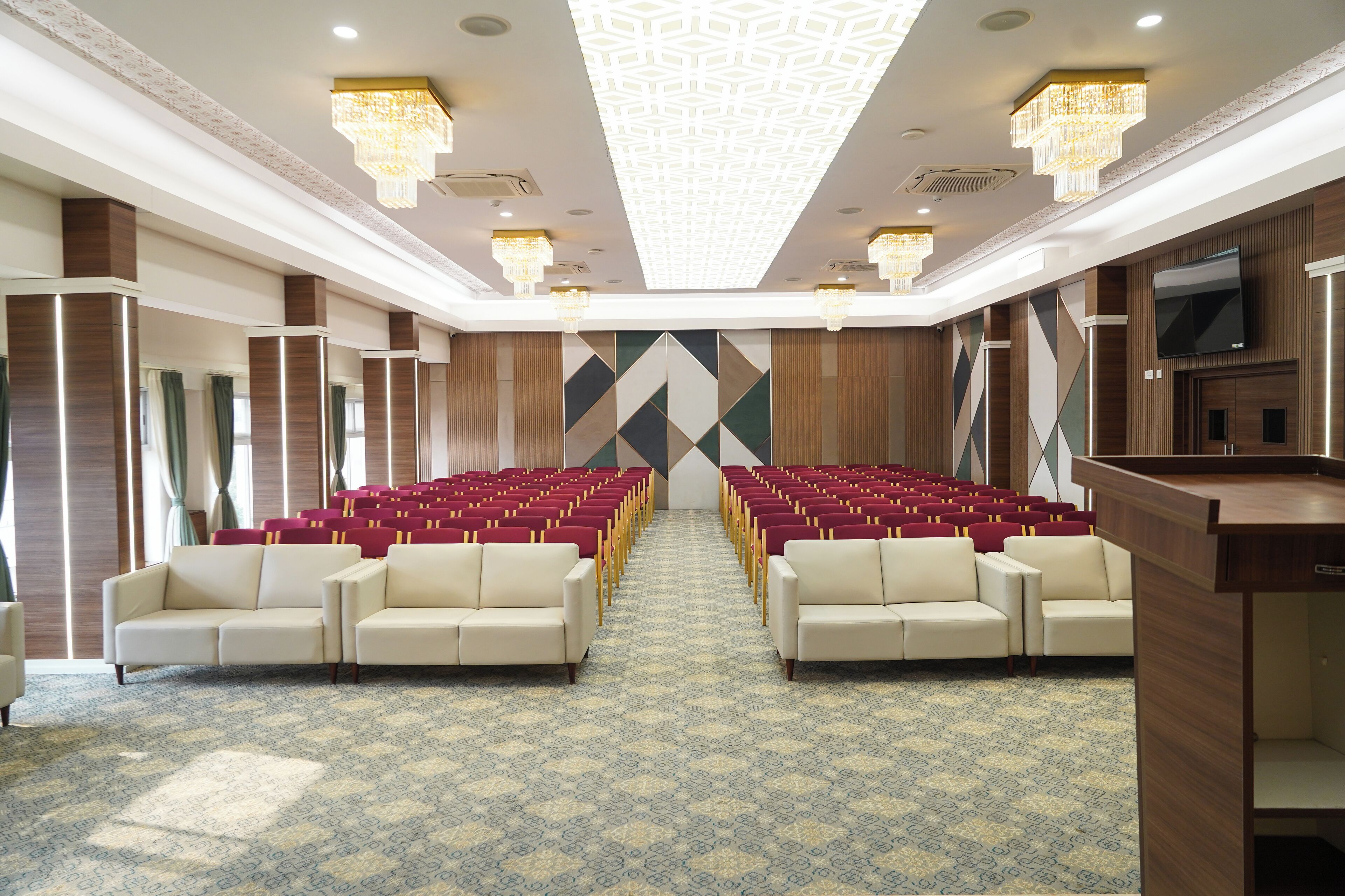 A conference room with rows of red and white chairs, a podium, and a large screen.