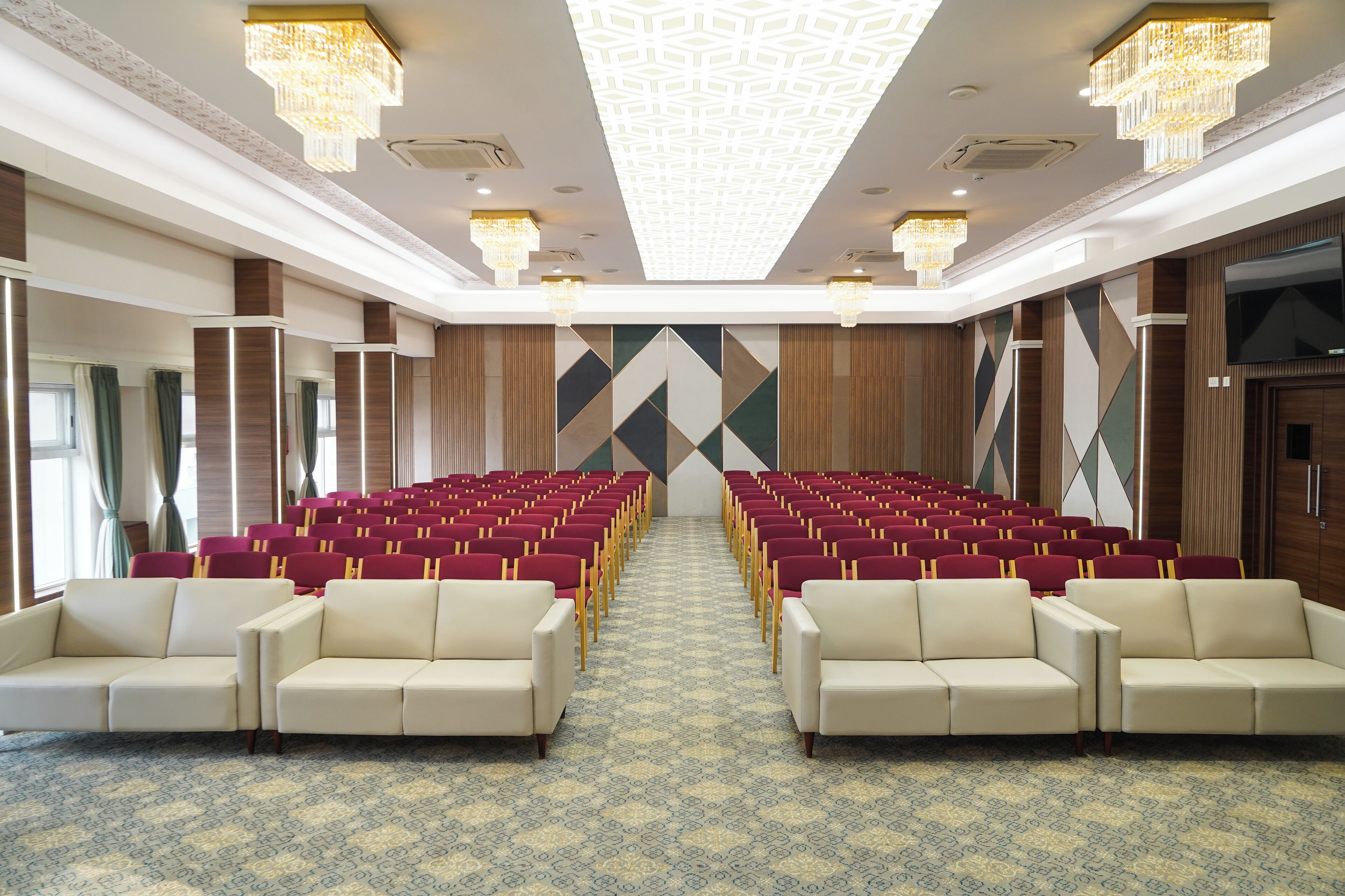 A conference room with rows of red and white chairs, a patterned carpet, and chandeliers.