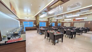 A spacious dining area with multiple tables and chairs, a buffet counter, and modern lighting fixtures. - Highland Hotel (Bengaluru)