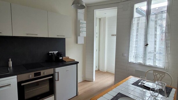 Een kleine keuken met een eethoek, houten vloeren en een raam met decoratieve gordijnen.