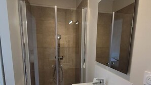 Een moderne badkamer met een douchecabine van glas, een witte wastafel met spiegel en een lamp boven de spiegel.
