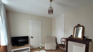 Een woonkamer met een flatscreen televisie, een witte salontafel, een beige fauteuil, een houten vloer en een donker houten kast met spiegel.