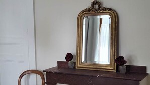 Een hoekzaak met een donker houten console, een spiegel met gouden lijst, en een houten stoel met een groene kussens.