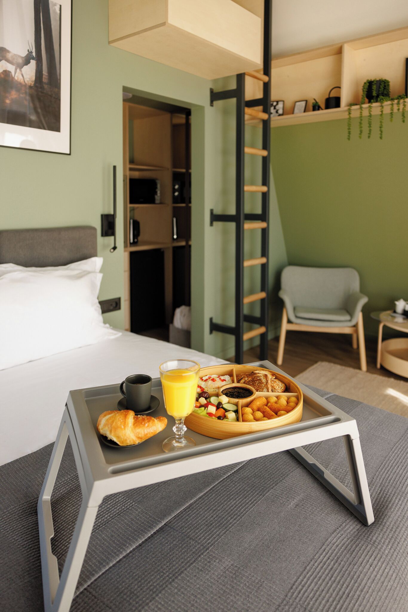 Un lit bien fait, avec un plateau contenant divers éléments pour le petit-déjeuner, notamment des croissants, des fruits et du jus.