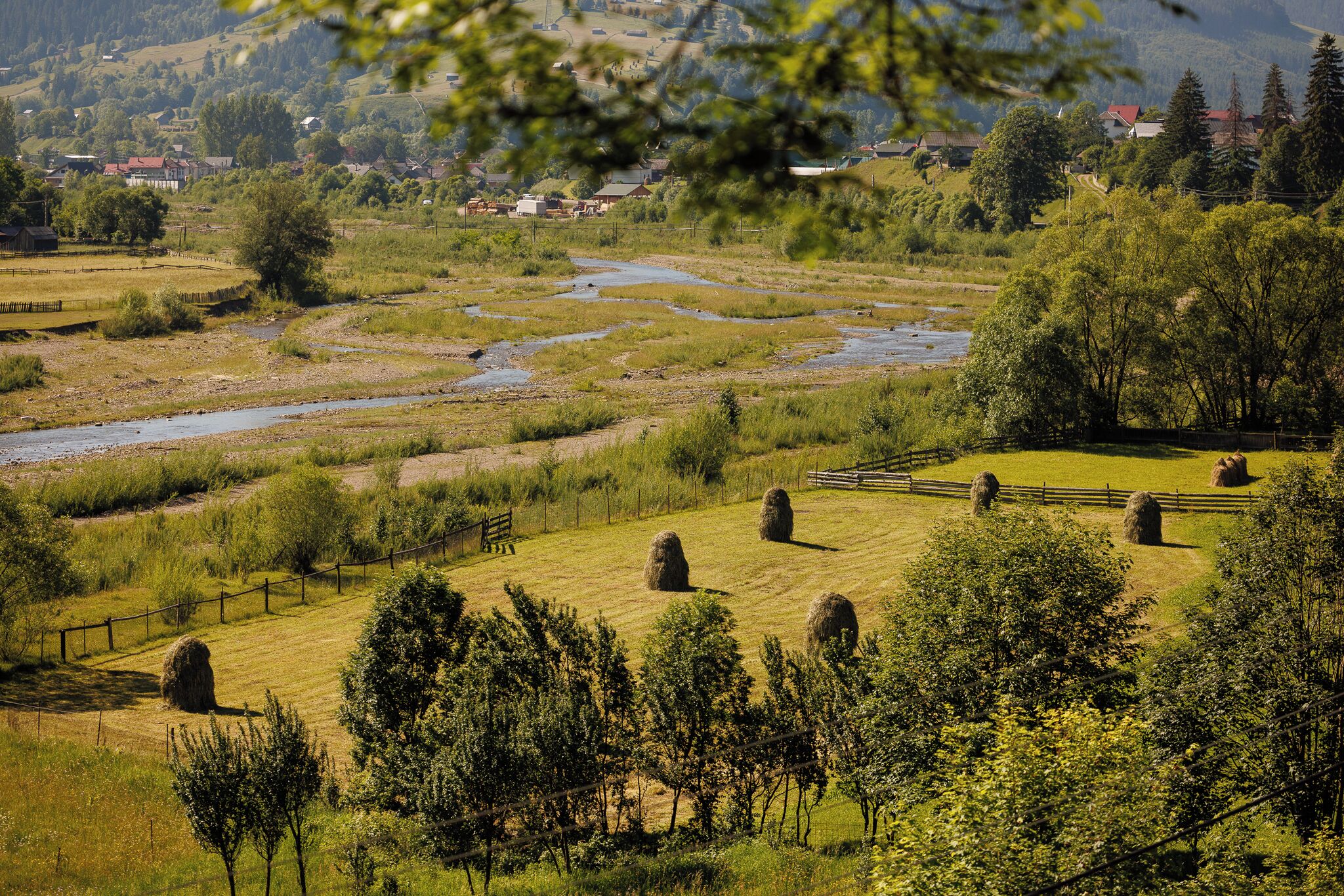 Een landelijk landschap met een rivier, hooibalen en een hek.