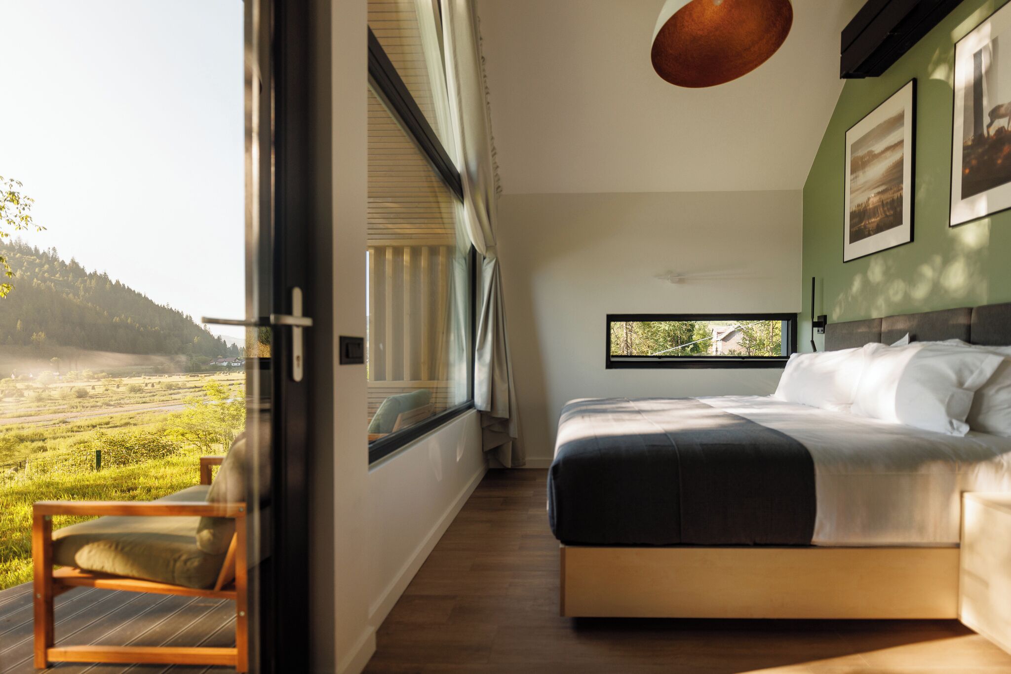 A bedroom with a large window, a bed, and a view of a landscape.