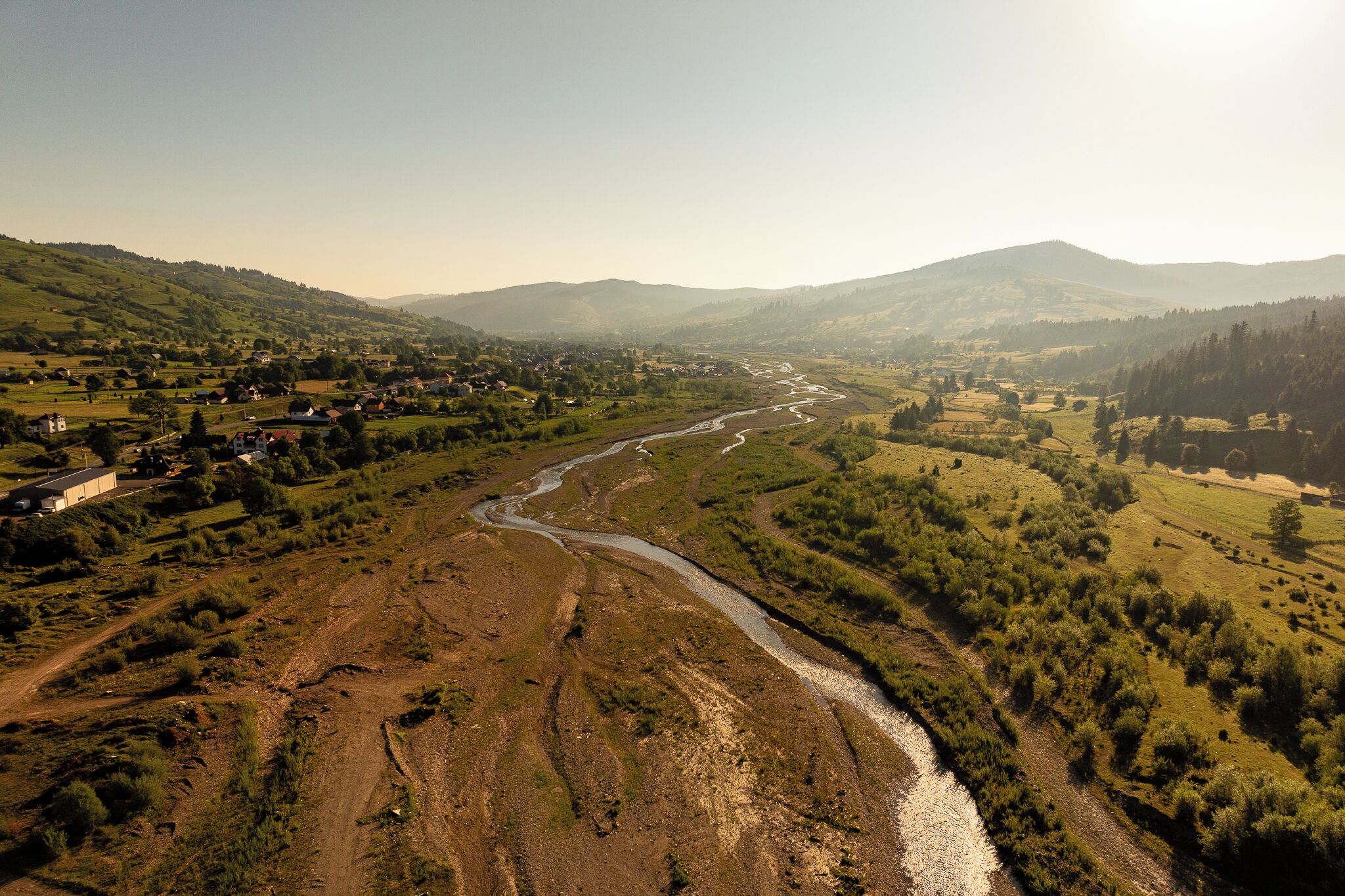 A river winding through a valley with hills on either side, surrounded by greenery and scattered buildings.