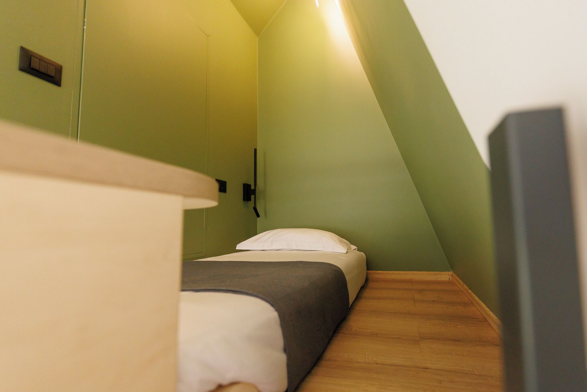 Una habitación pequeña y estrecha con cama, suelo de madera y paredes verdes.