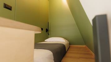 Una habitación pequeña y estrecha con cama, suelo de madera y paredes verdes.